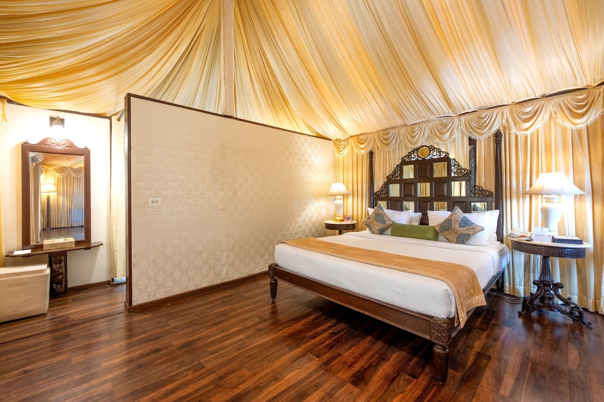 Une chambre d’hôtel spacieuse, dotée d’un grand lit, d’un parquet, d’un miroir et d’une table de chevet avec une lampe.