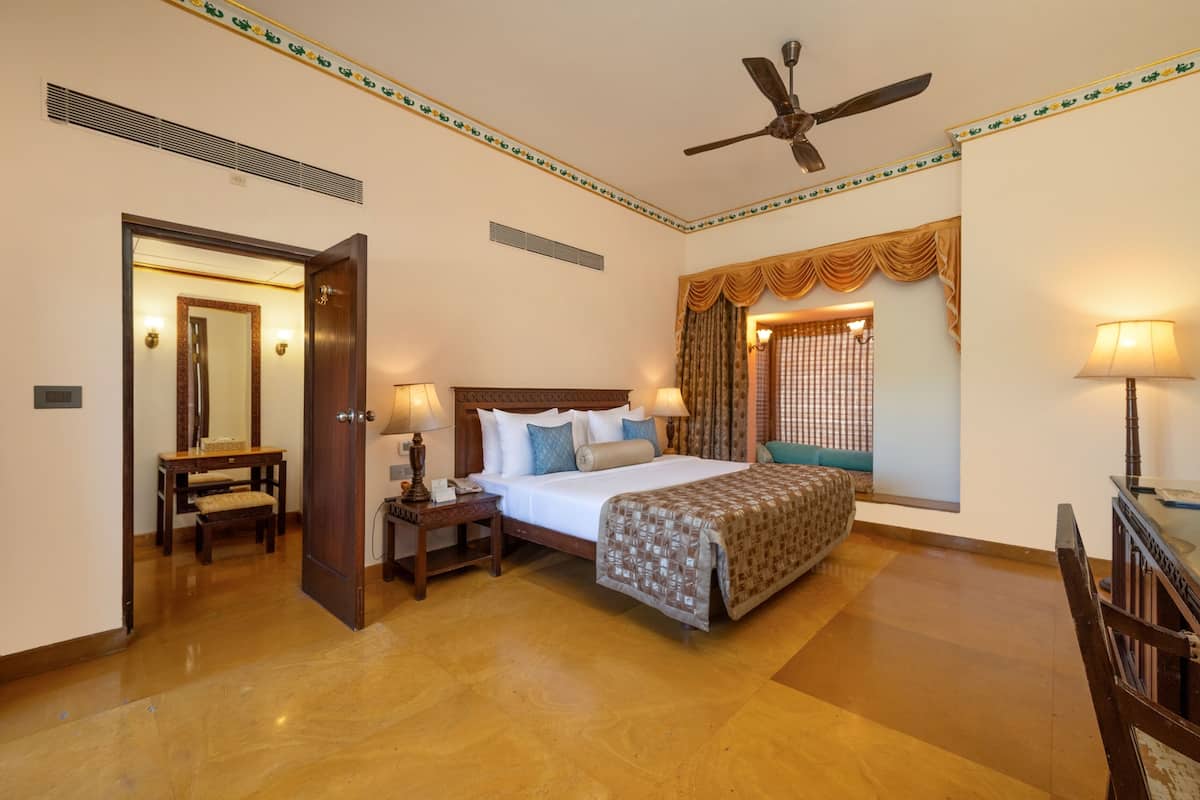 Une chambre d’hôtel comprenant un lit, des tables de chevet, un bureau, une chaise, un ventilateur de plafond et une fenêtre avec des rideaux.