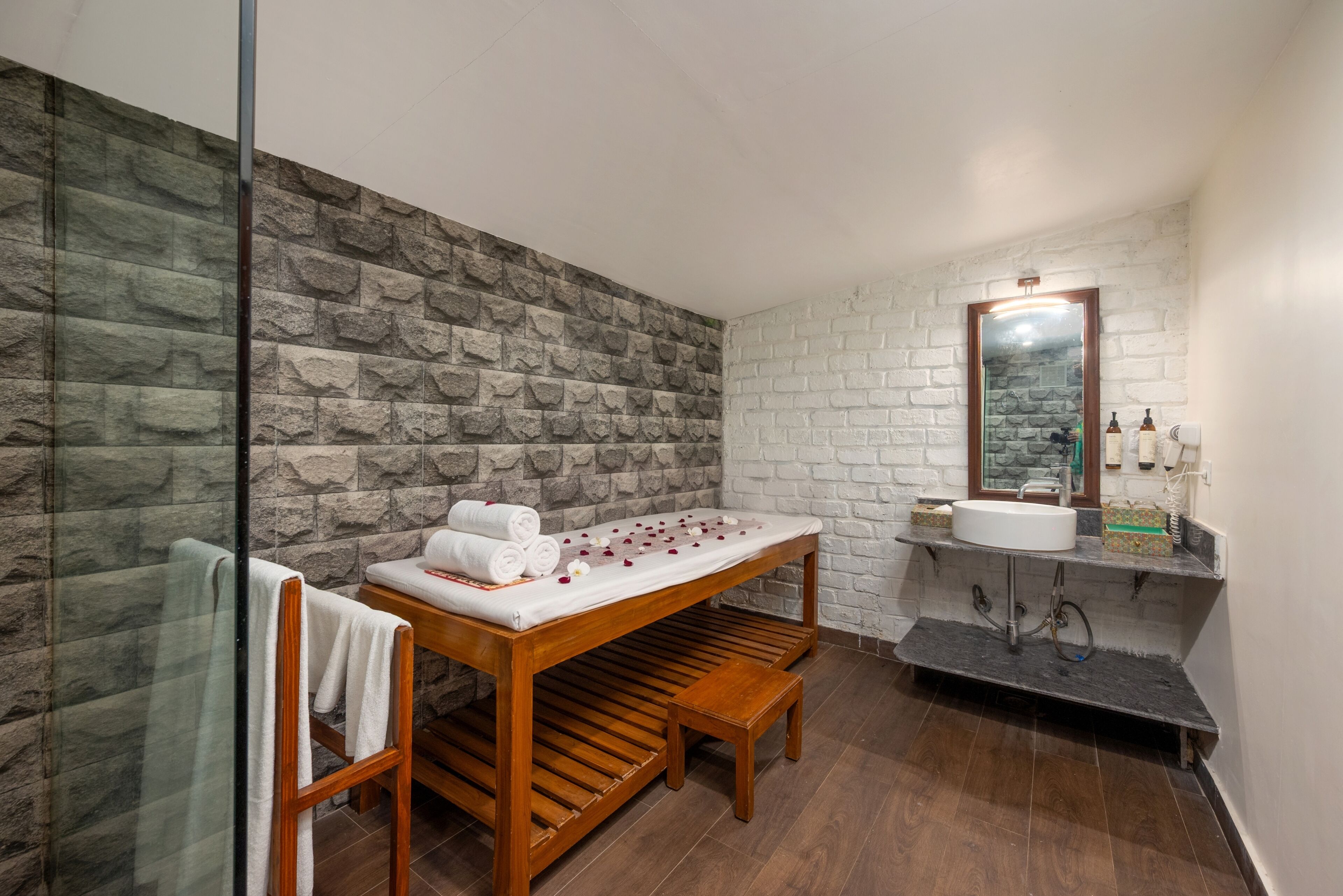 A bathroom with a stone wall, a wooden bench, a sink, and a mirror.