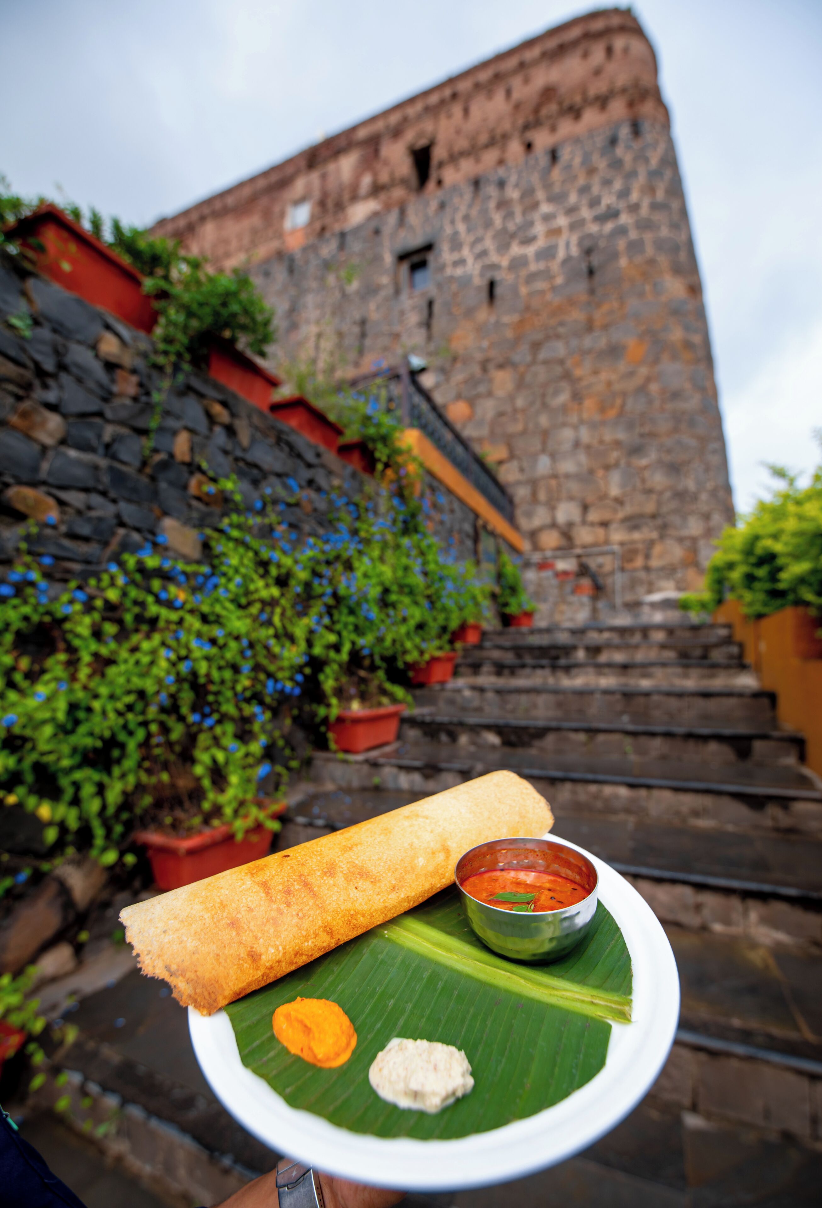A traditional dish on a banana leaf with a stone building in the background.