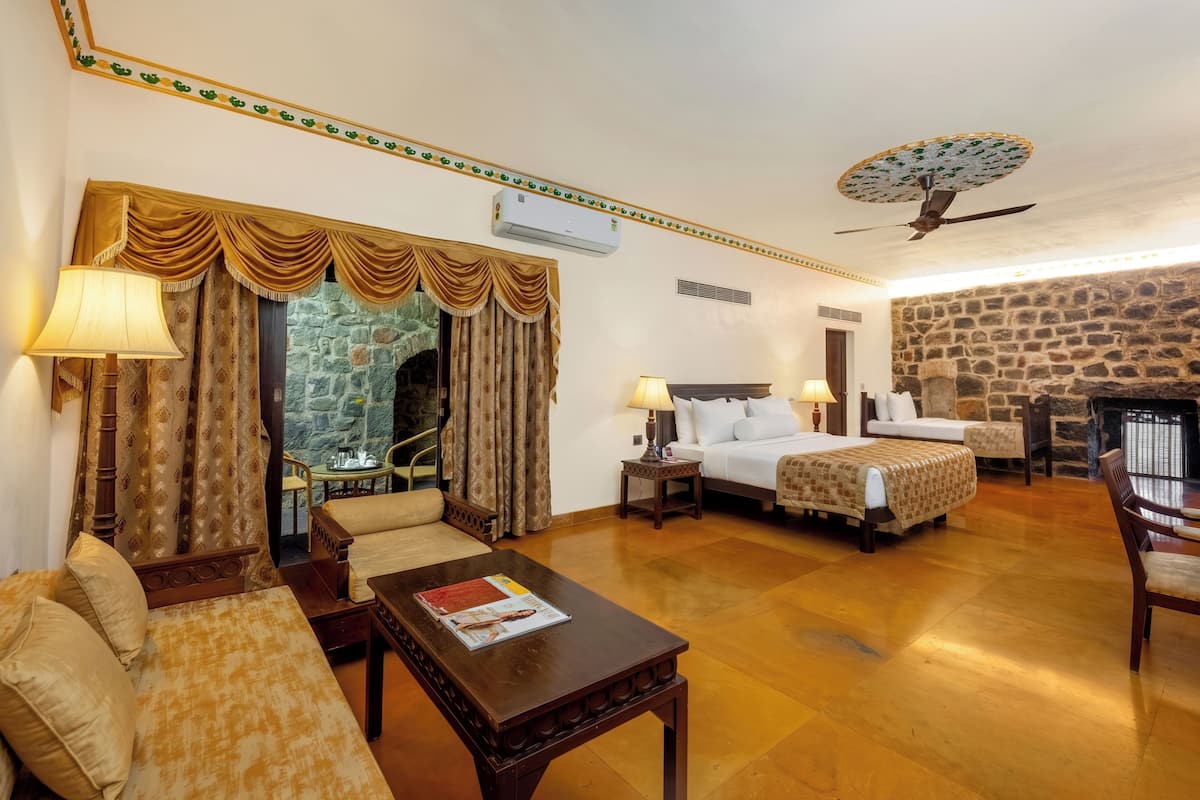 Une chambre d’hôtel avec un mur en pierre, un lit, un canapé, une table basse et un coin repas.
