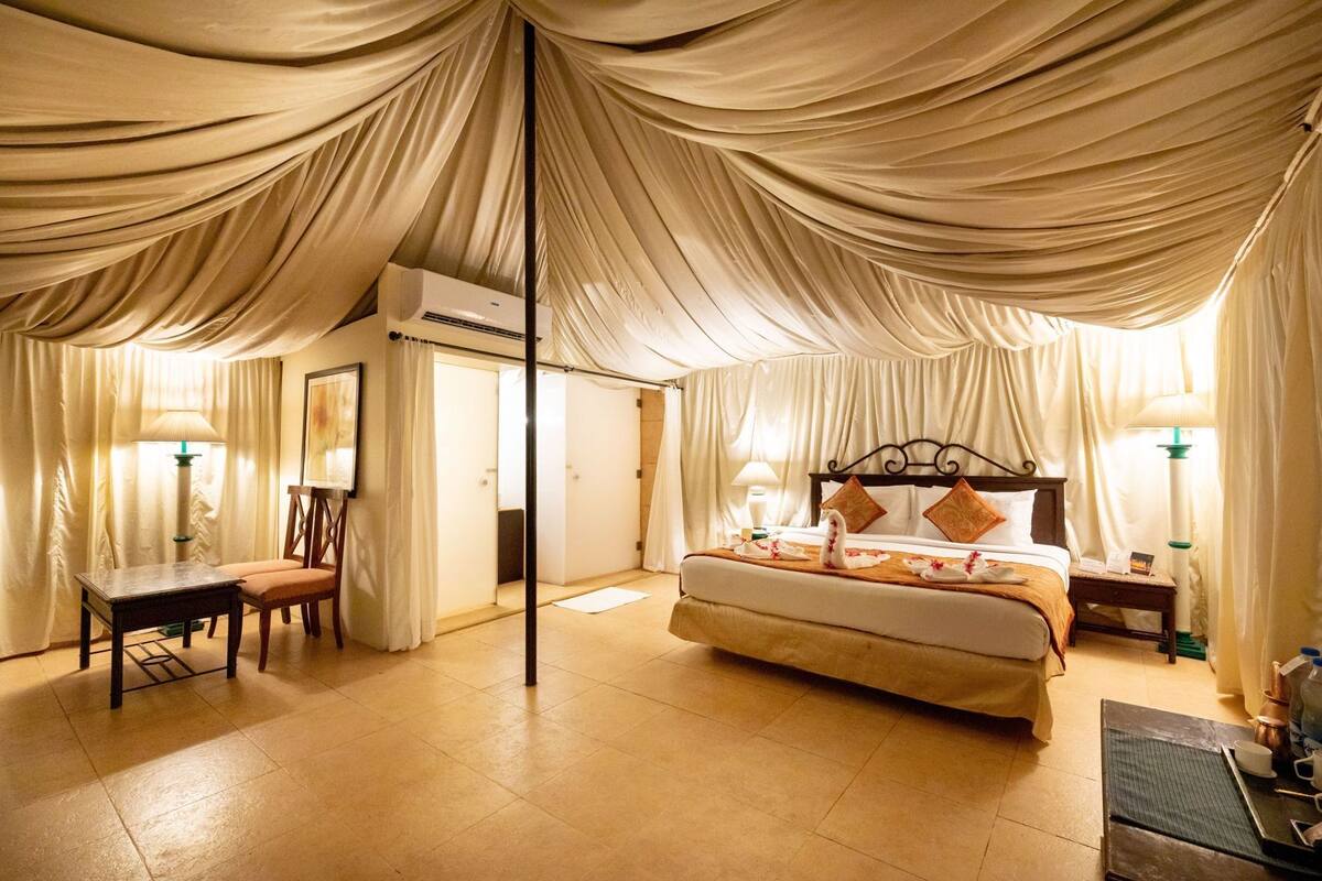 Une chambre spacieuse avec un grand lit, un bureau et une chaise, le tout sous un plafond décoré de tentures.