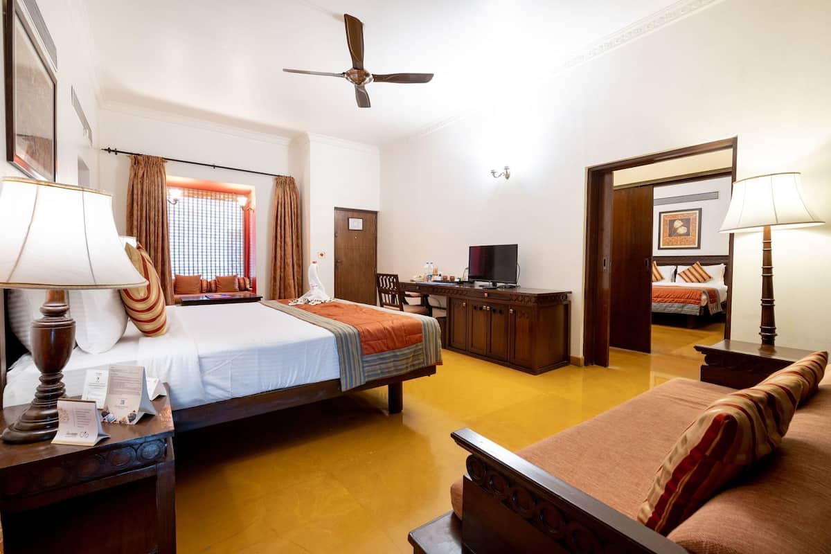 Une chambre d’hôtel comprenant un lit, un bureau avec une télévision, un canapé, un ventilateur de plafond et une porte donnant sur une autre pièce.