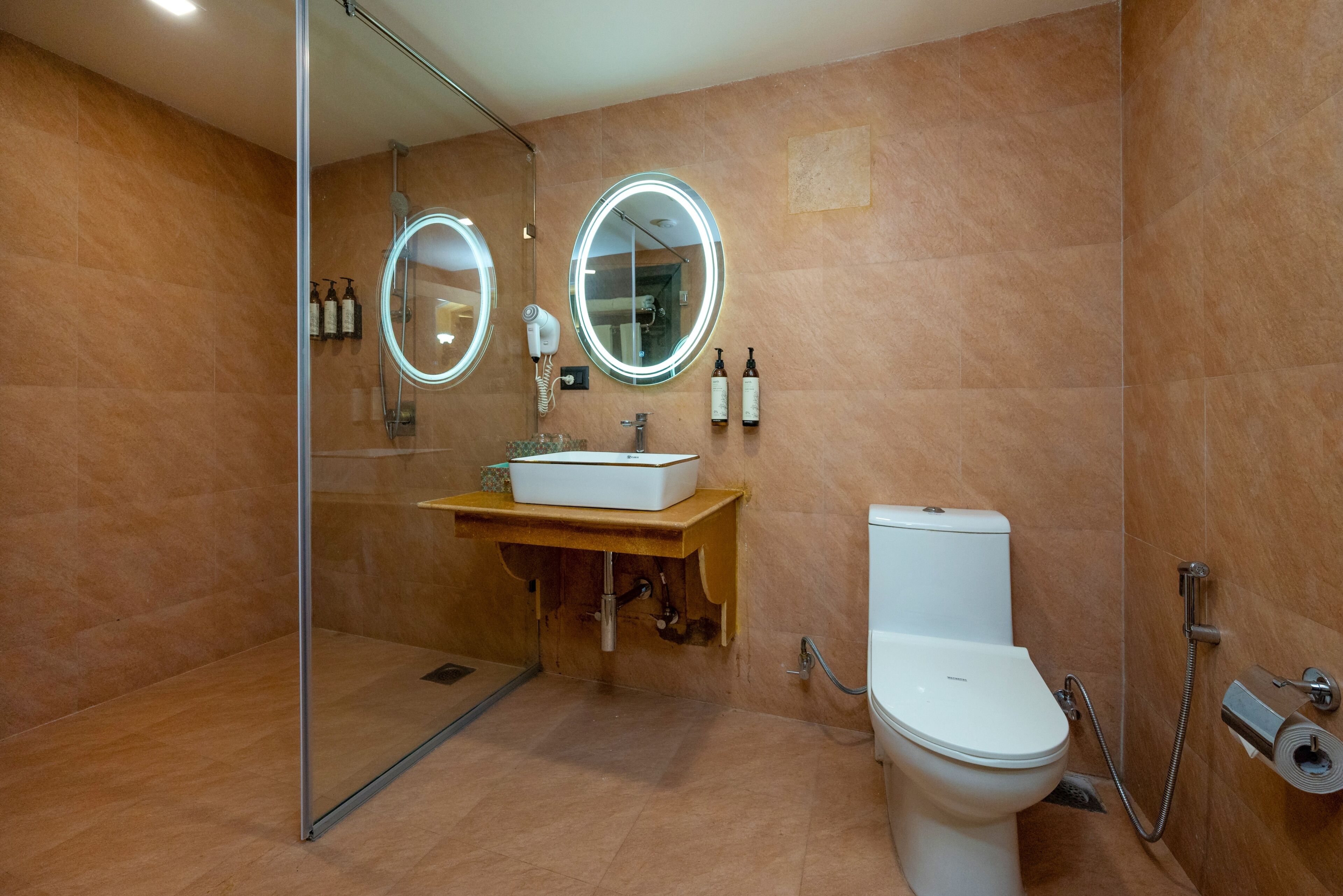 A modern bathroom with a glass shower enclosure, a white sink with a wooden countertop, a toilet, and two illuminated mirrors.