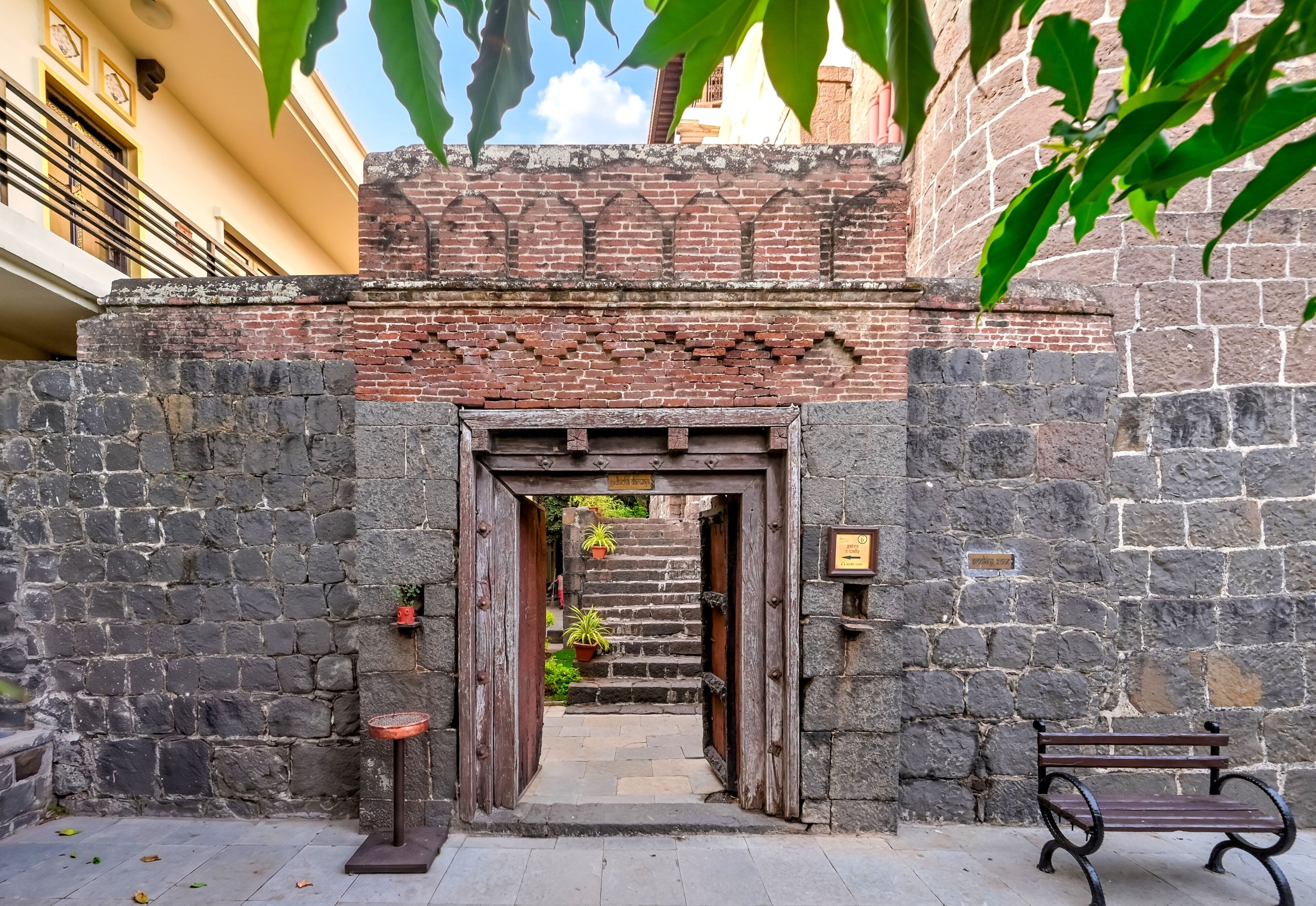A stone archway leading to a courtyard with a bench and potted plants.