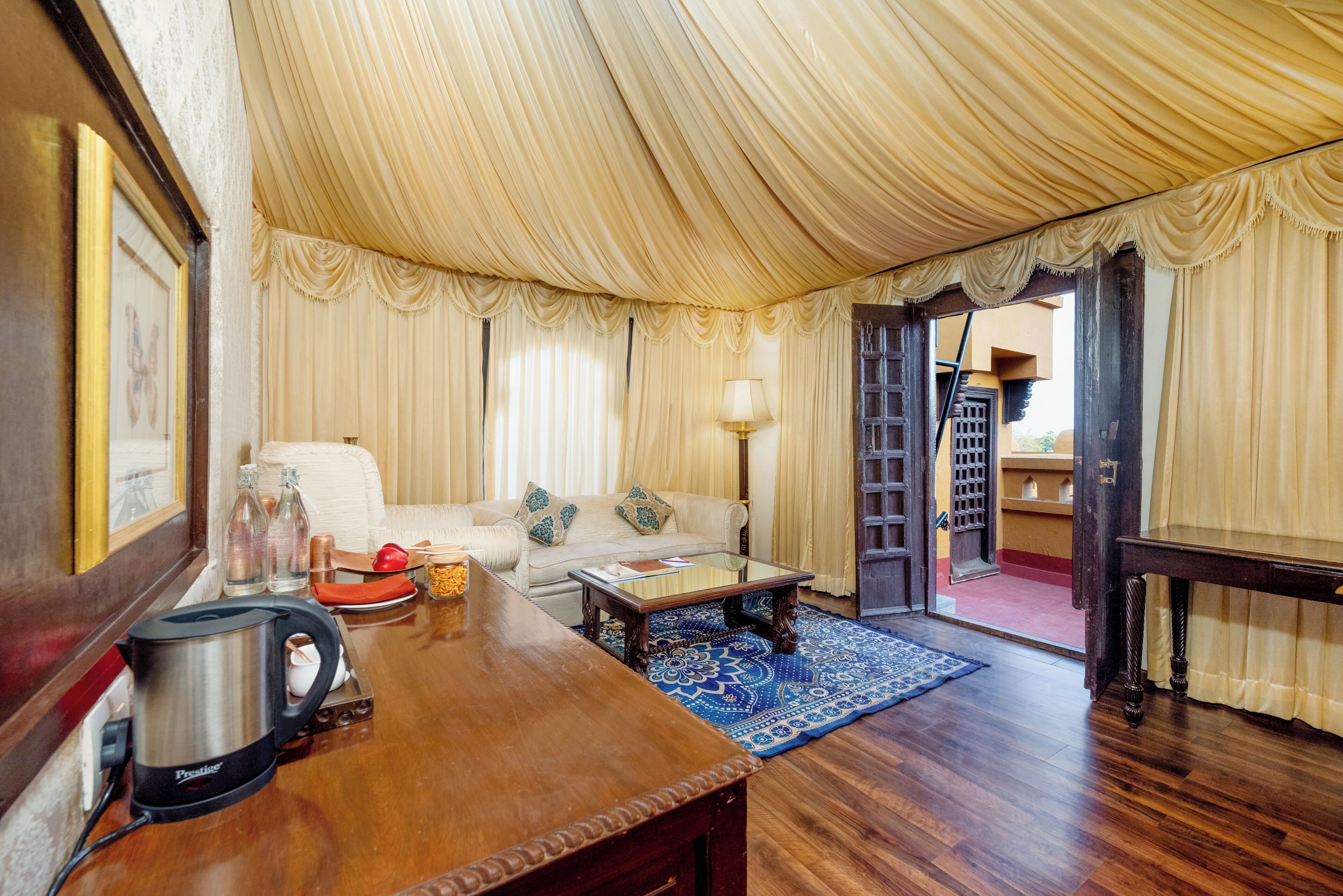 Una habitación con una mesa de centro de madera, un sofá, una lámpara, un hervidor y una alfombra estampada.