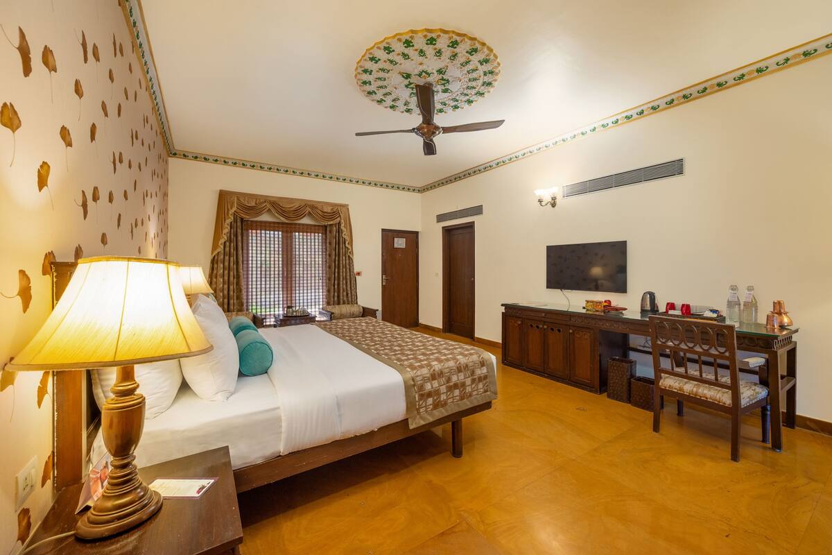 Une chambre d’hôtel équipée d’un lit, d’un bureau, d’une chaise, d’un ventilateur de plafond et d’une télévision.