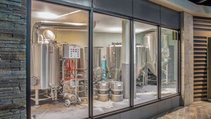 Una cervecería con tanques de acero inoxidable, equipo de elaboración y barriles visibles a través de amplios ventanales.