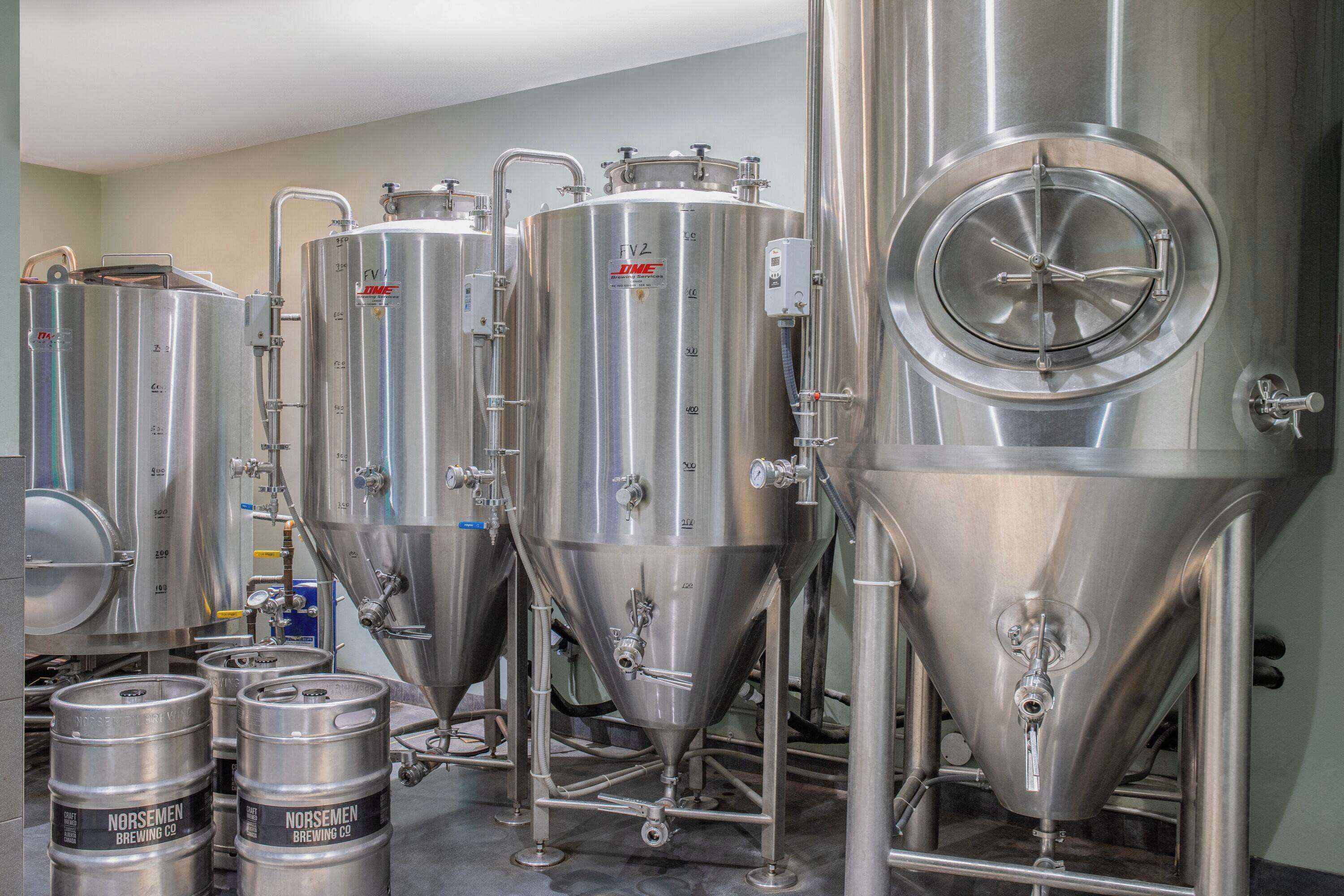 Stainless steel brewing tanks and kegs in a brewery setting.