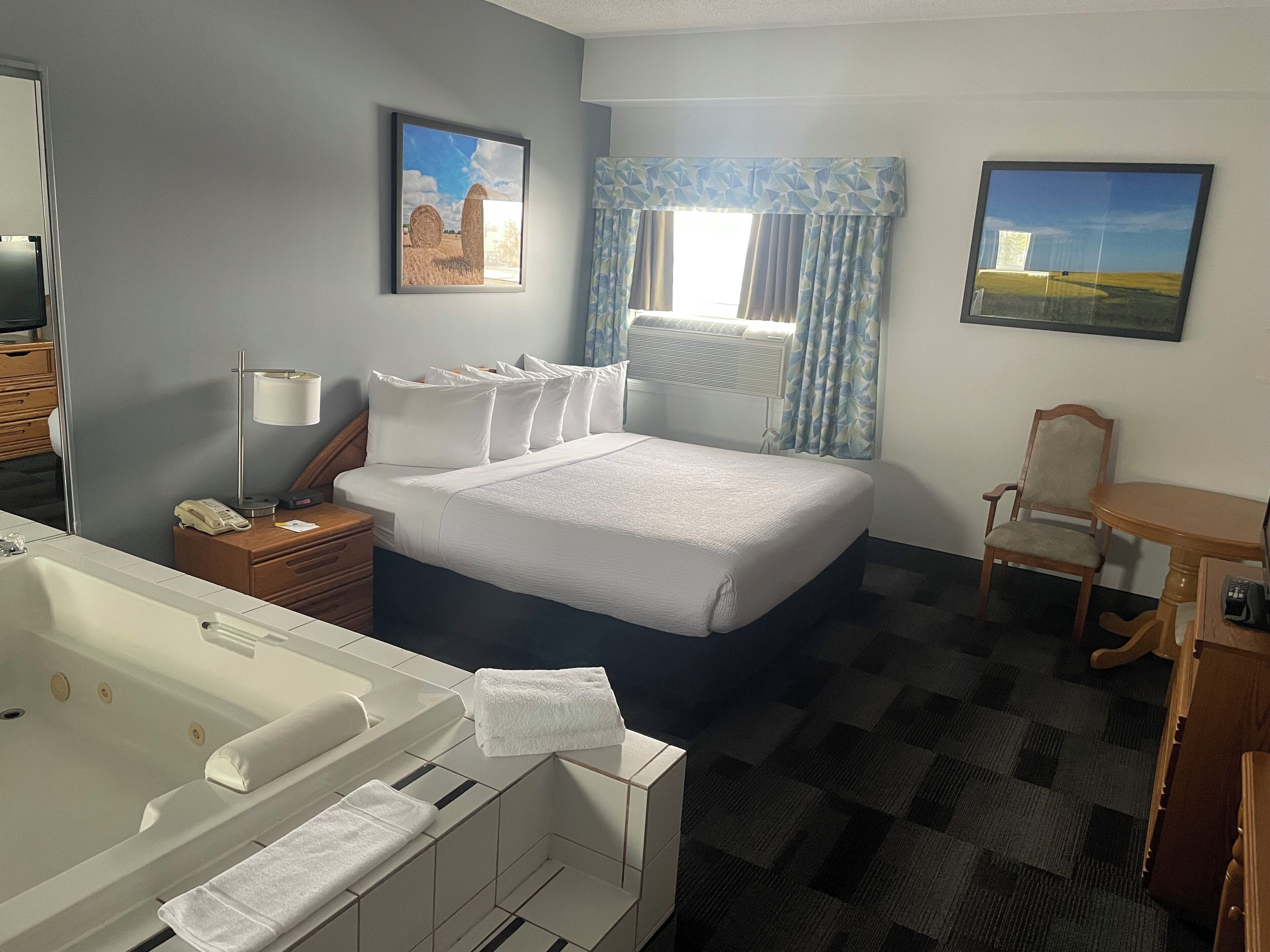 Habitación de hotel con una cama grande, baño con bañera, escritorio y dos cuadros en la pared.