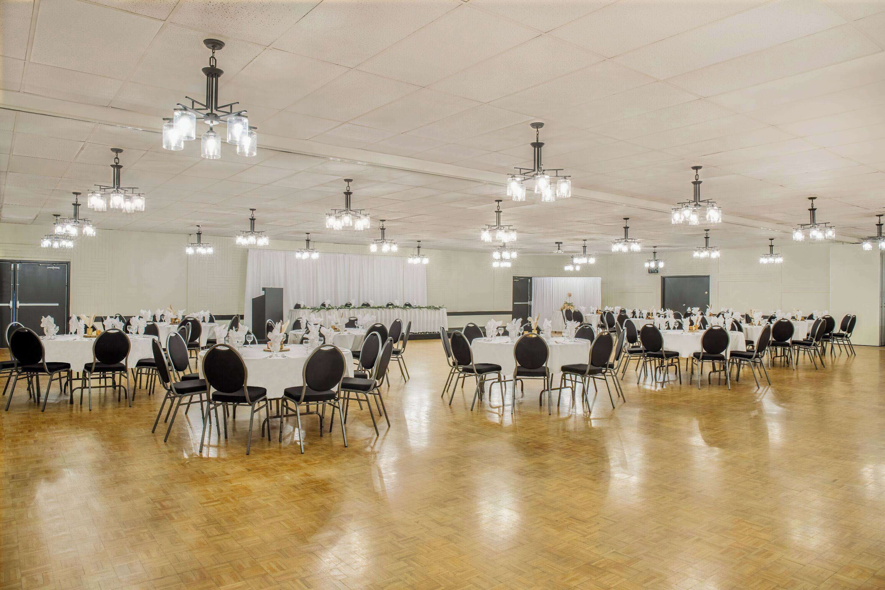 Ein großer Saal mit mehreren Tischen und Stühlen, die in Reihen angeordnet sind, mit Kronleuchtern an der Decke.