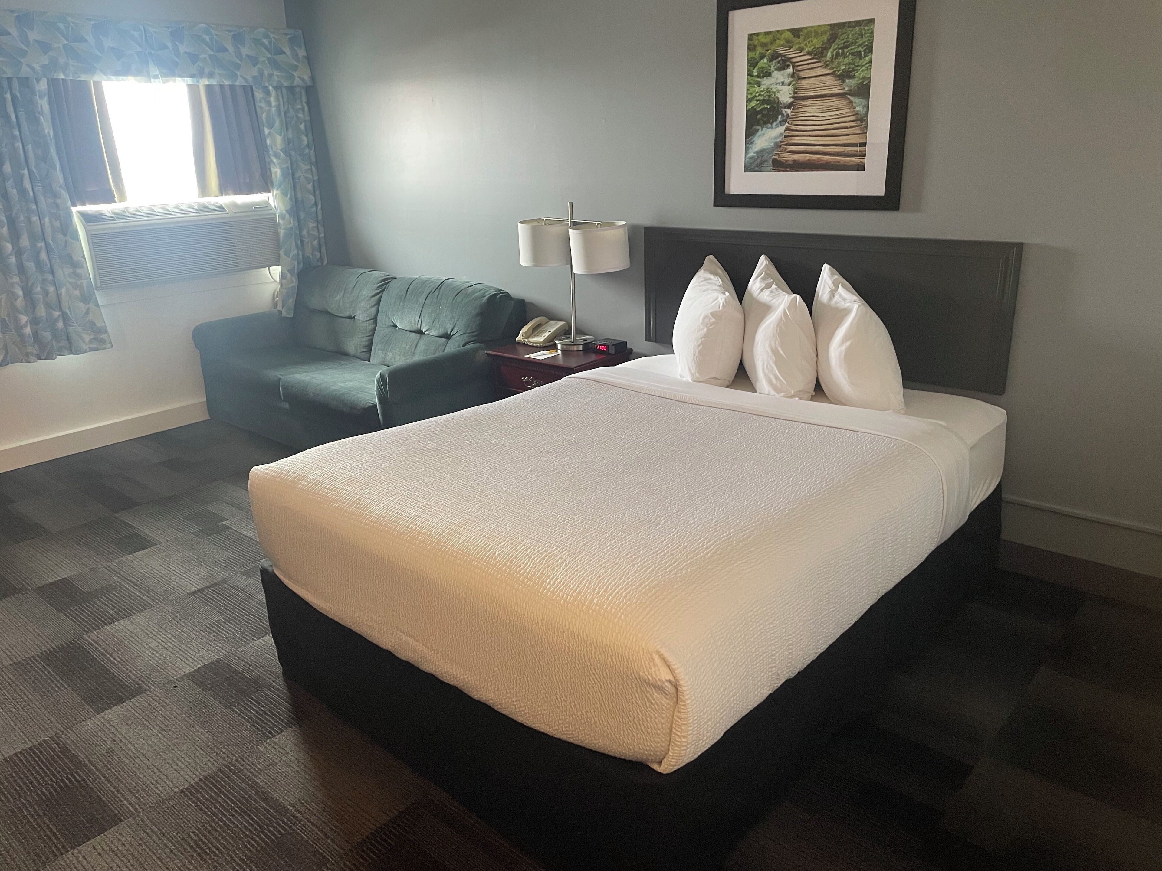 Una habitación de hotel con una cama grande, un escritorio con lámpara, una silla y una ventana con cortinas.