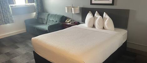 Una habitación de hotel con una cama grande, un escritorio con lámpara, una silla y una ventana con cortinas.