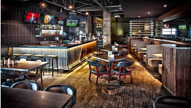 Un bar moderno con mostrador, varias televisiones y diferentes distribuciones de asientos.