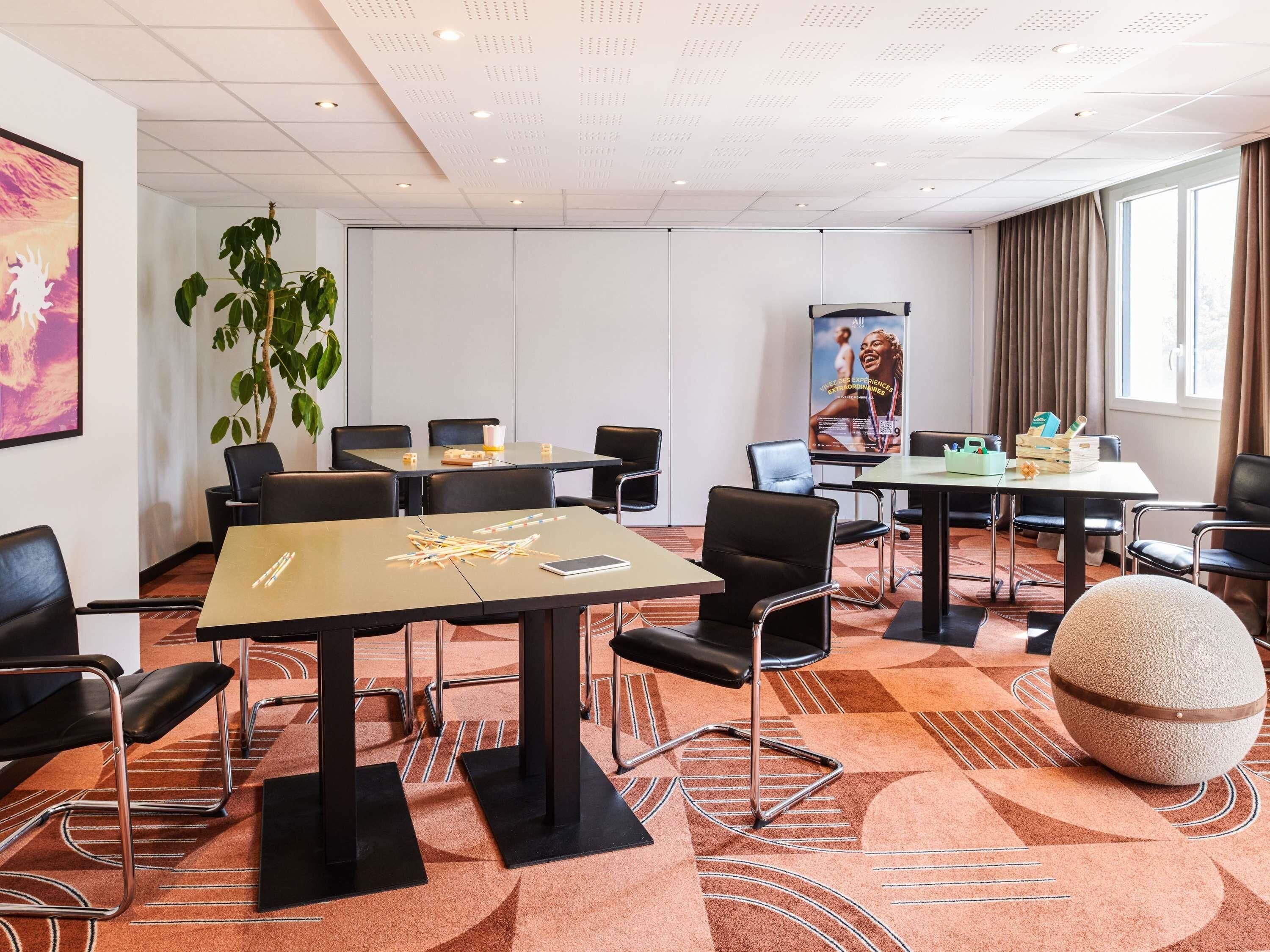 A conference room with tables, chairs, a large plant, and a poster on the wall.