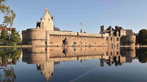 Un castillo histórico con un foso, un ciclista y un reflejo claro en el agua.