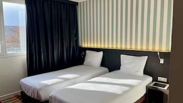 Habitación de hotel con dos camas, una ventana con cortinas, un muro a rayas y una mesita de noche pequeña.