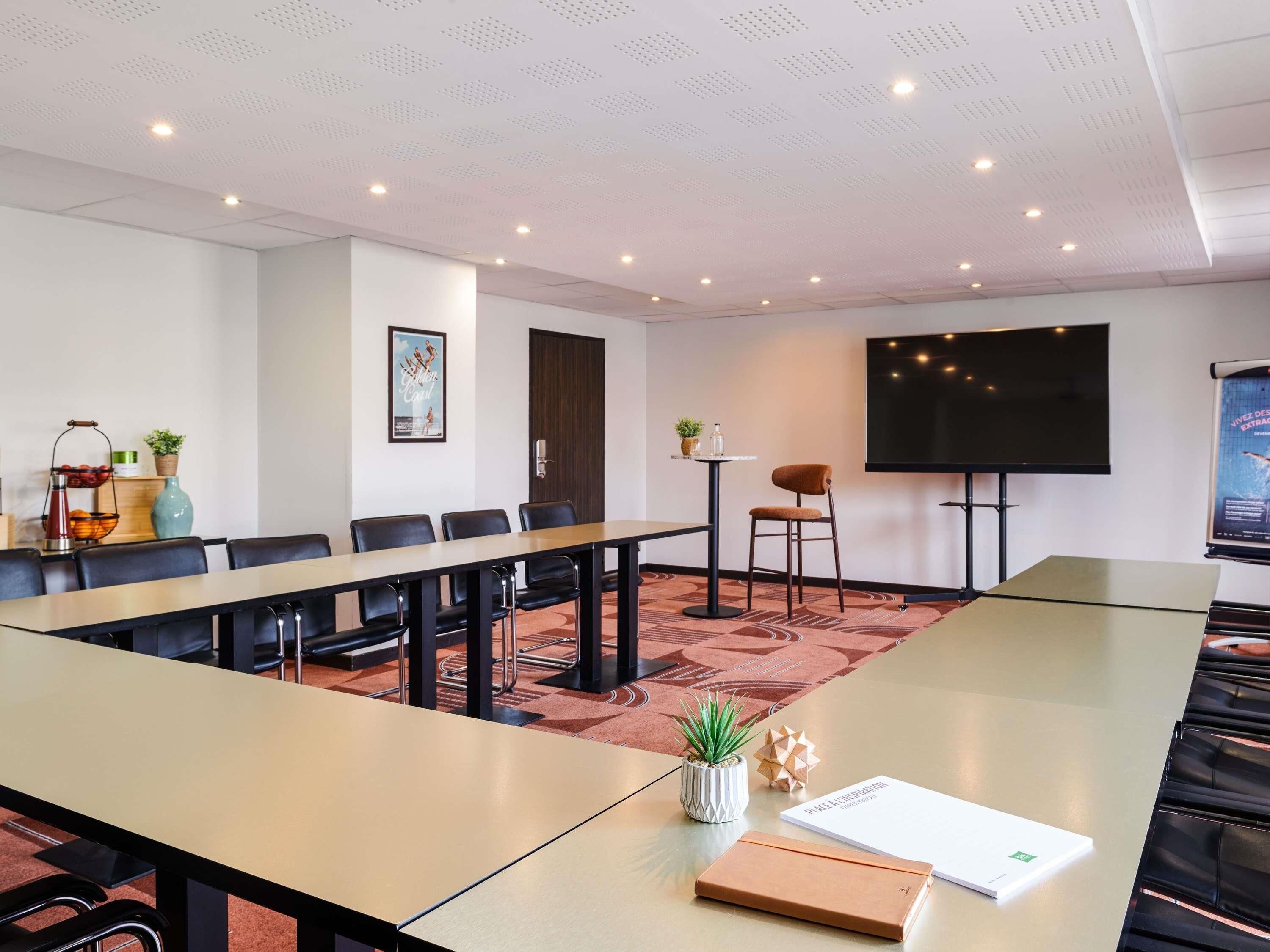 A conference room with a long table, chairs, a projector screen, and a television.