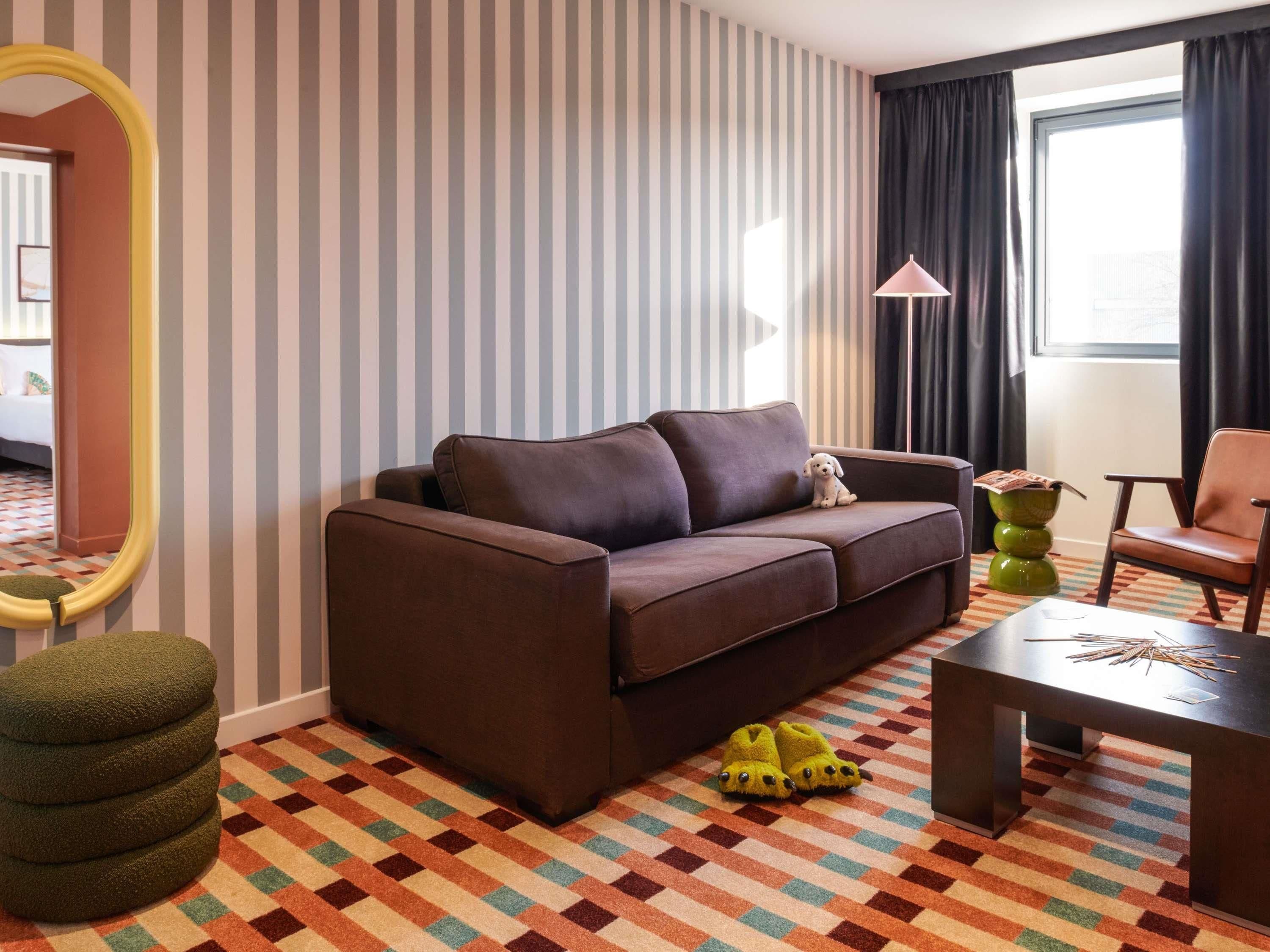 Un salon moderne avec un canapé, une petite table, un fauteuil, un miroir et un tapis à motifs.