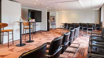 A conference room with a large screen, black leather chairs, a small table with a plant, and a patterned carpet.