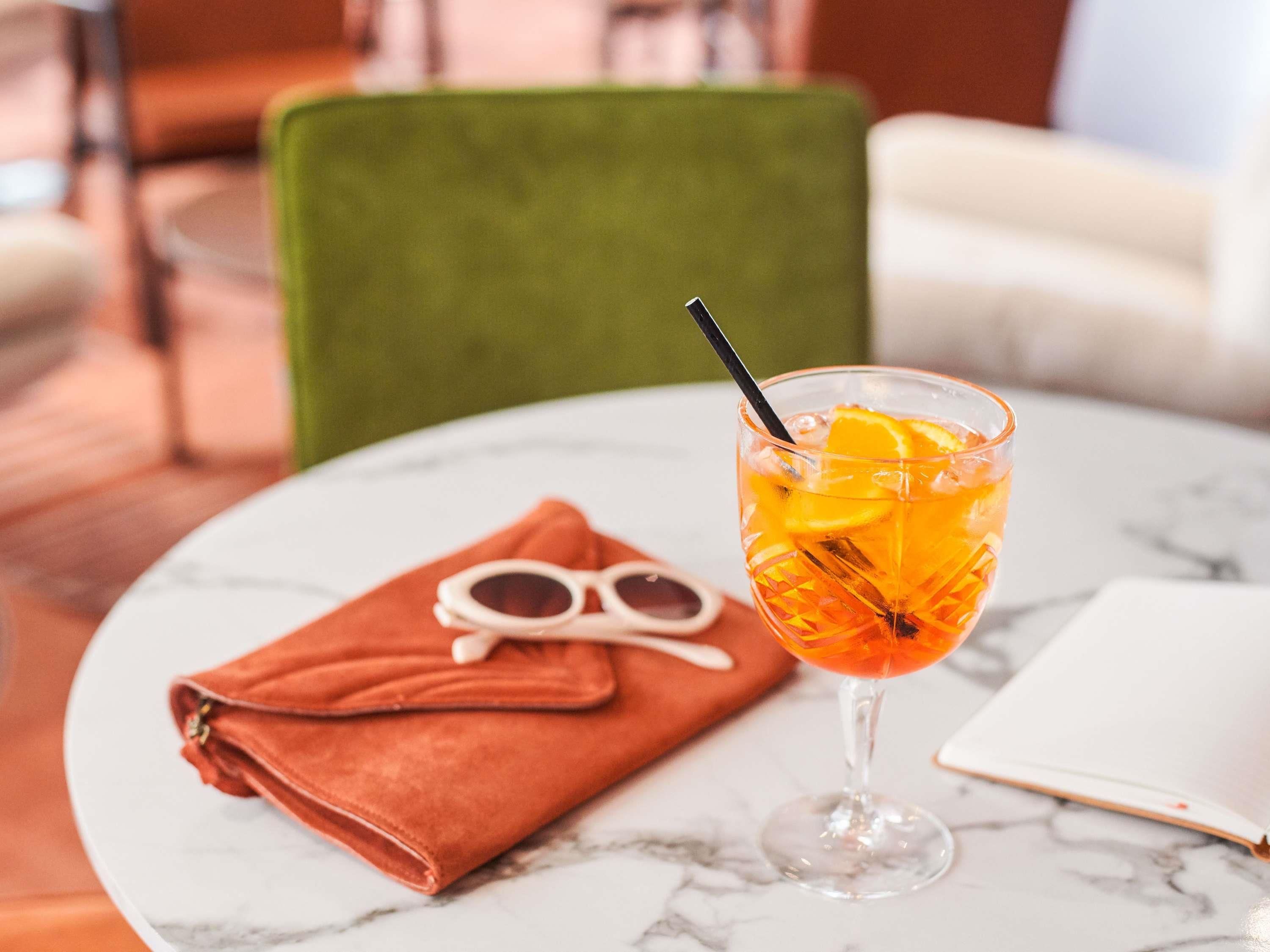 A table with a glass of orange juice, a pair of sunglasses, and a brown napkin.