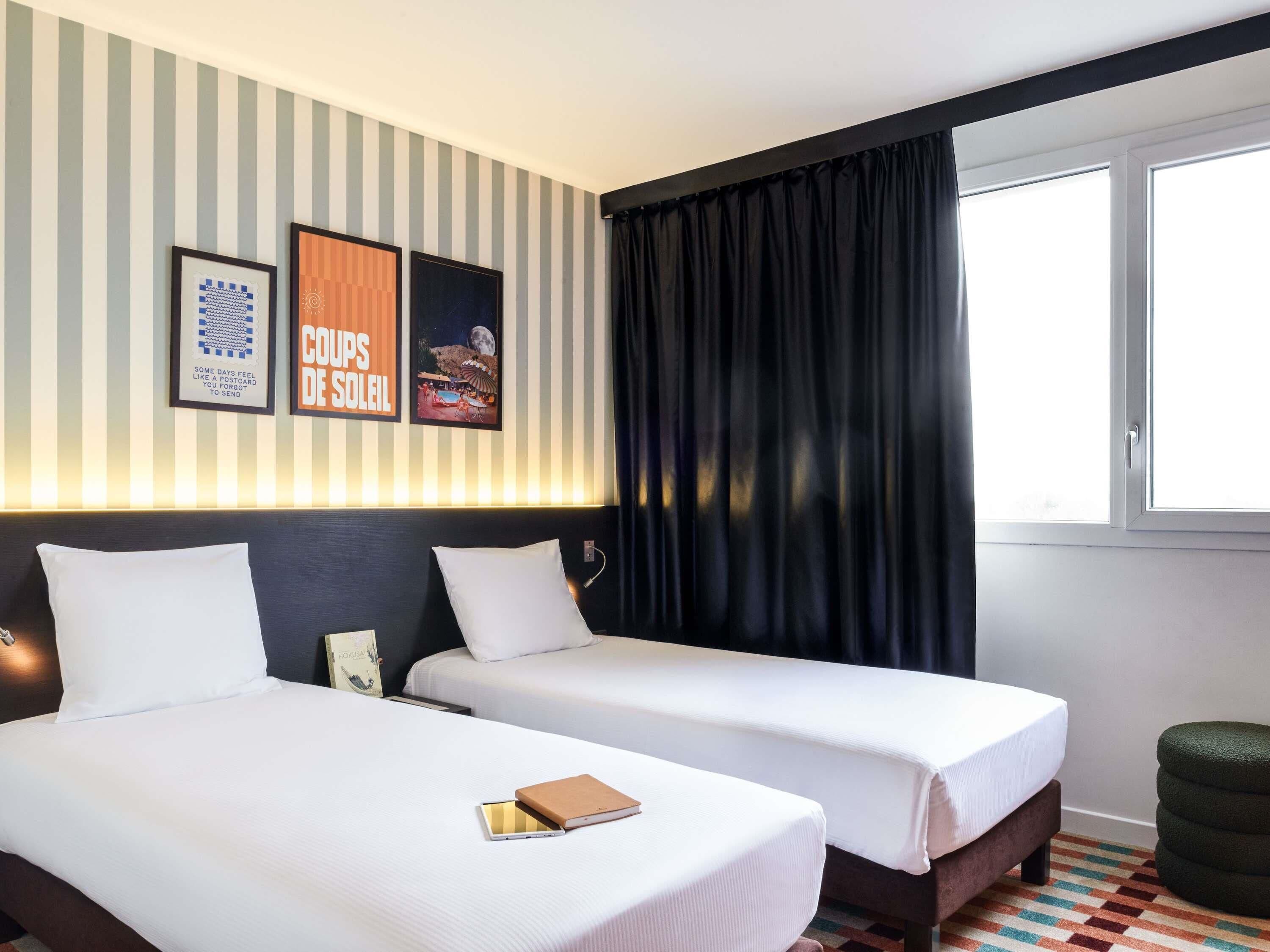 A hotel room with two beds, a window with black curtains, and striped wallpaper.