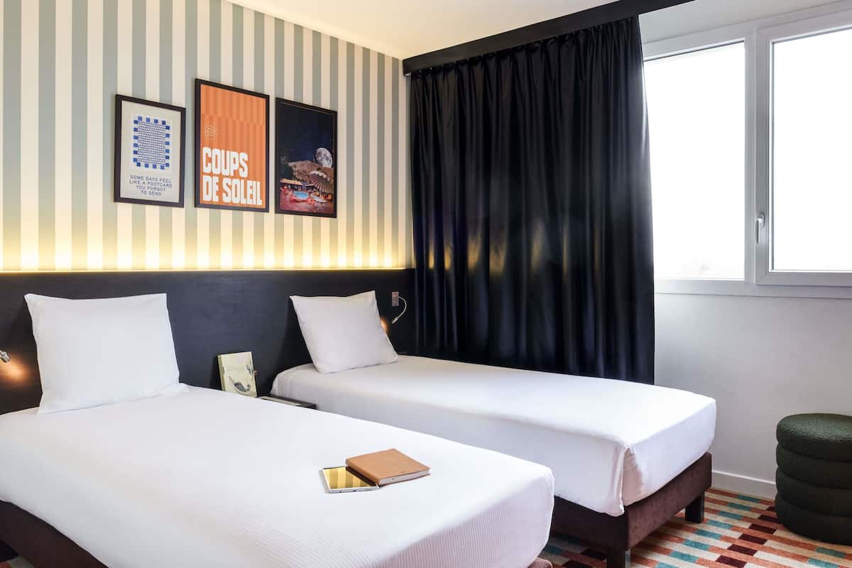 A hotel room with two beds, a window with black curtains, and striped wallpaper.