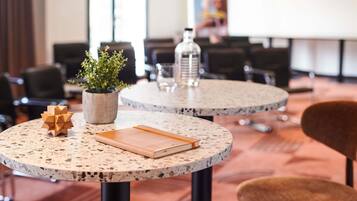 A conference room with round tables, chairs, a potted plant, a water bottle, and a poster on the wall.
