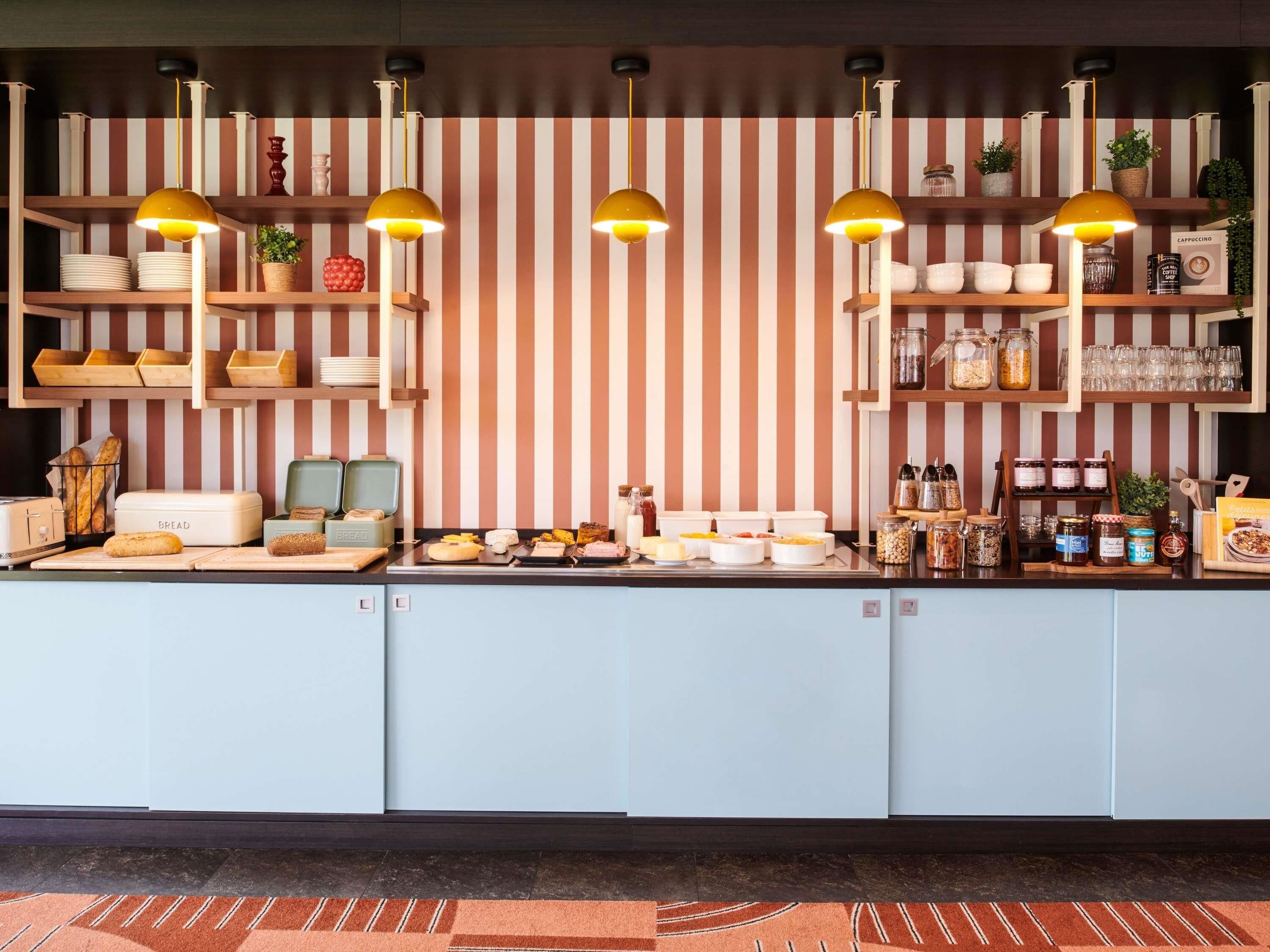 Un bar de petit-déjeuner avec un papier peint à rayures, des suspensions lumineuses et divers aliments.