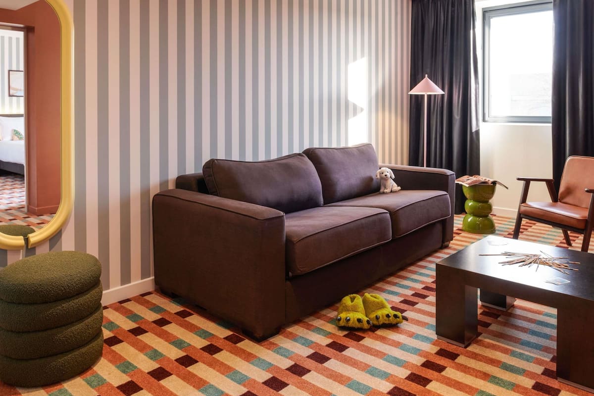 A modern living room with a sofa, a small table, a chair, a mirror, and a patterned carpet.