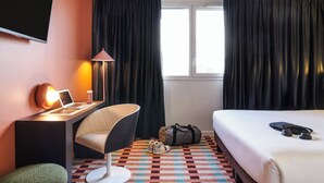 A hotel room with a bed, a desk with a laptop, a chair, a lamp, a TV, and a window with curtains. - ibis Styles Nantes Saint Herblain (Saint-Herblain)