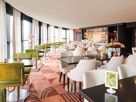 Restaurante moderno com várias áreas de estar, incluindo mesas redondas e cabines, além de um bar com diversas opções de comida e bebidas.