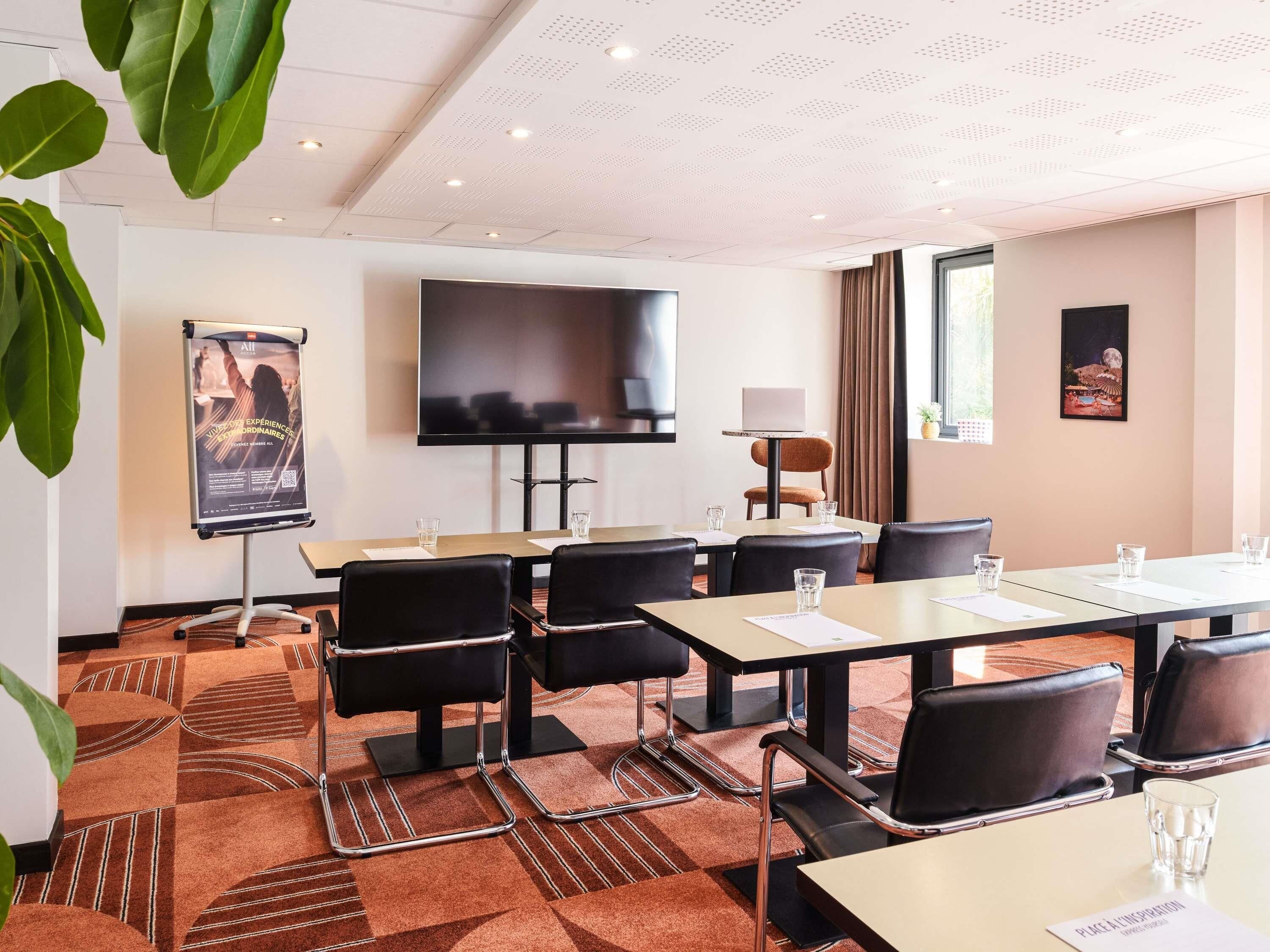 Un salón de conferencias con una pantalla plana grande, un cartel y una mesa con sillas.