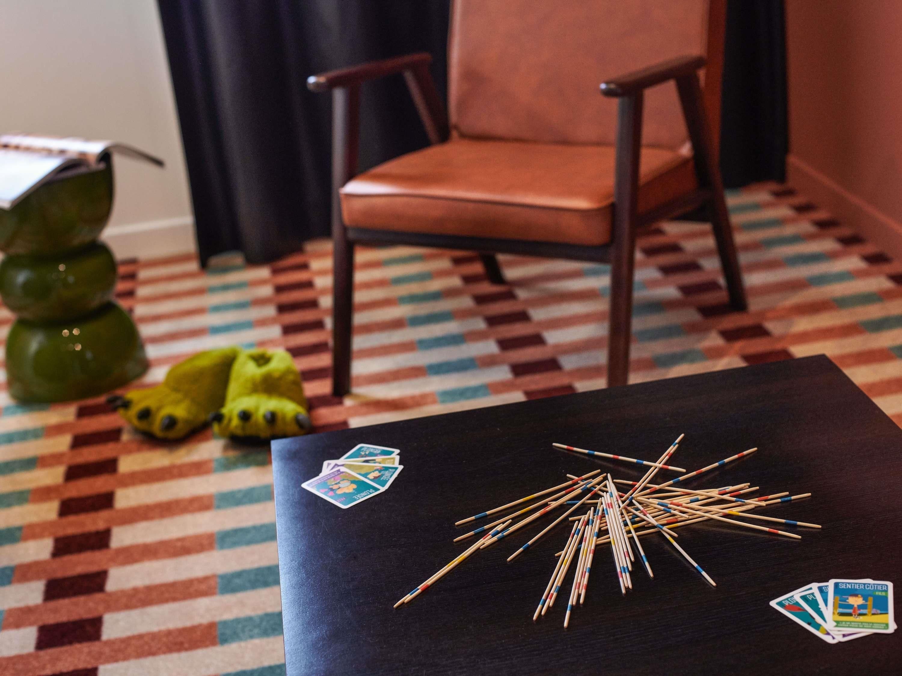A room with a checkered floor, a black table with matchsticks and playing cards, a brown chair, and a green plant.