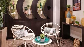 A modern interior with two white wicker chairs, a small round table with a green tray, and a dark wooden wall with glass shelves displaying decorative items.