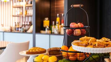 A dining area with a buffet setup including fruits, pastries, and a cake.