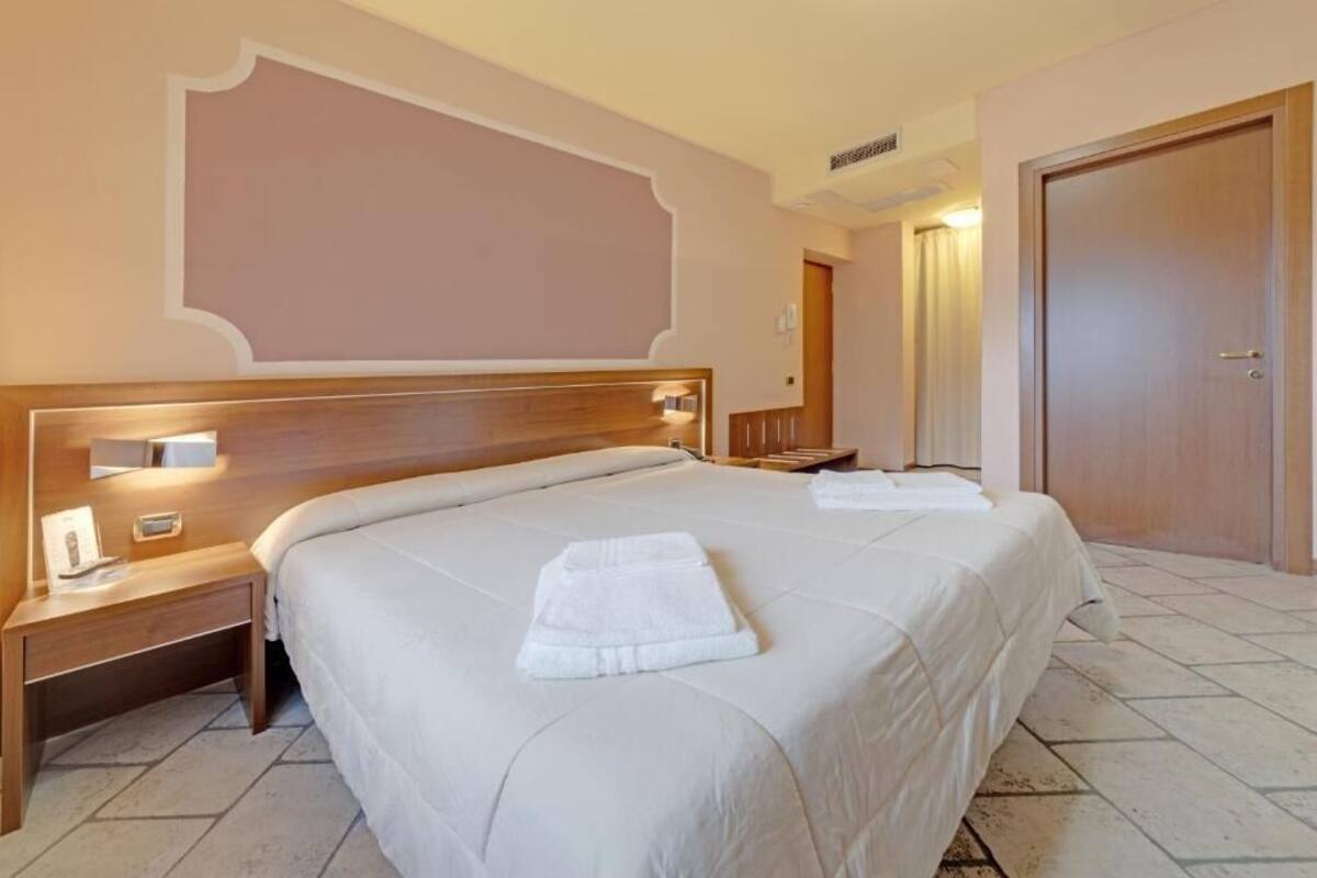 Een hotelkamer met een groot bed, een houten hoofdeinde, een nachtkastje en een deur.