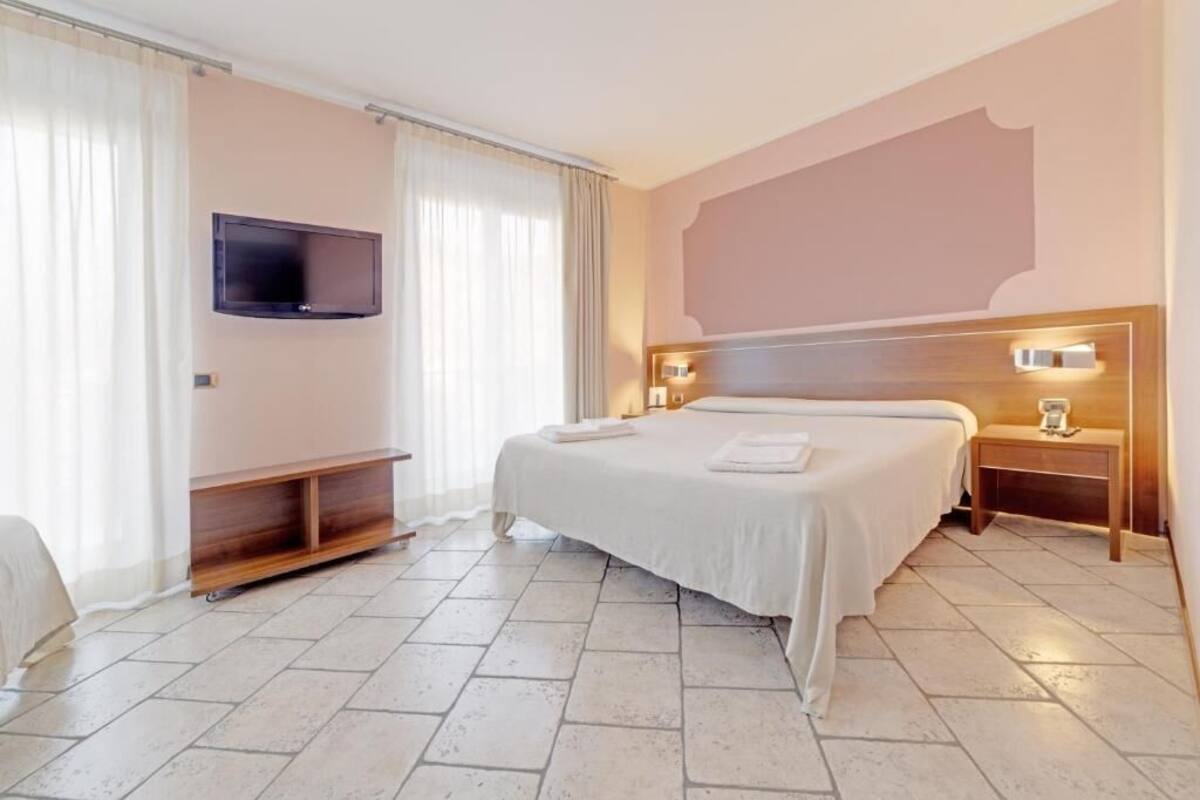 Hotelkamer met een groot bed, een flatscreen televisie aan de muur, een nachtkastje met een lamp en een houten bankvoet.