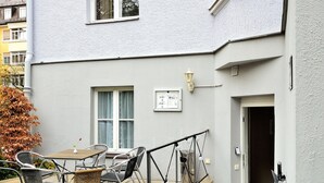 Un edificio con balcón, mesas al aire libre y una escalera que conduce a la entrada.