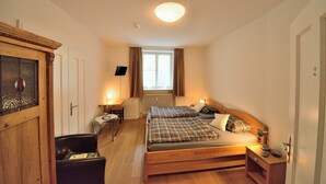 Un dormitorio con cama de madera, escritorio, silla, radiador y ventana con cortinas.
