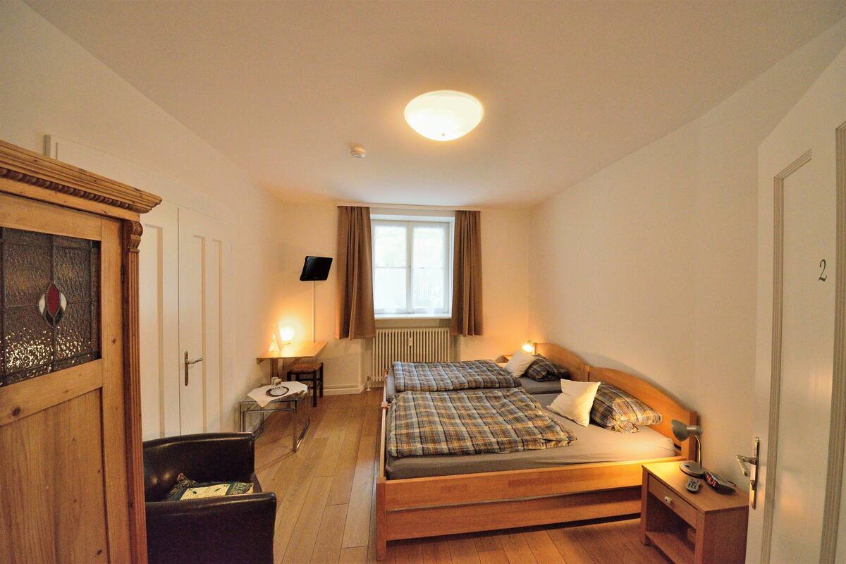 A bedroom with a wooden bed, a desk, a chair, a radiator, and a window with curtains.