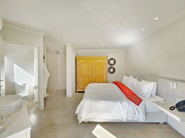 A bedroom with a bed, a bedside table with a phone, a wardrobe, and a shower area.