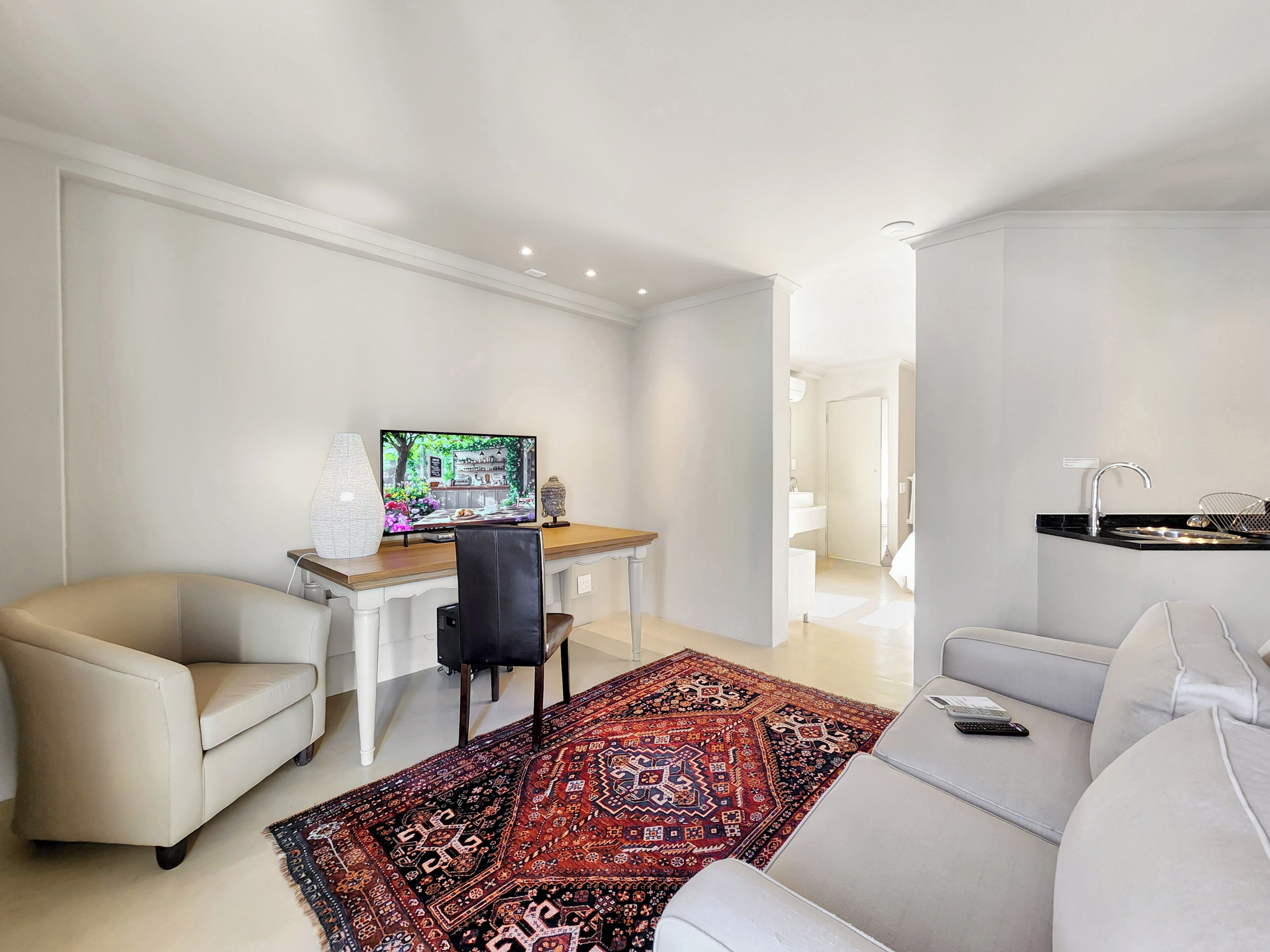 A modern living room with a flat-screen TV, a dining table, a sofa, and a kitchen area with a sink.
