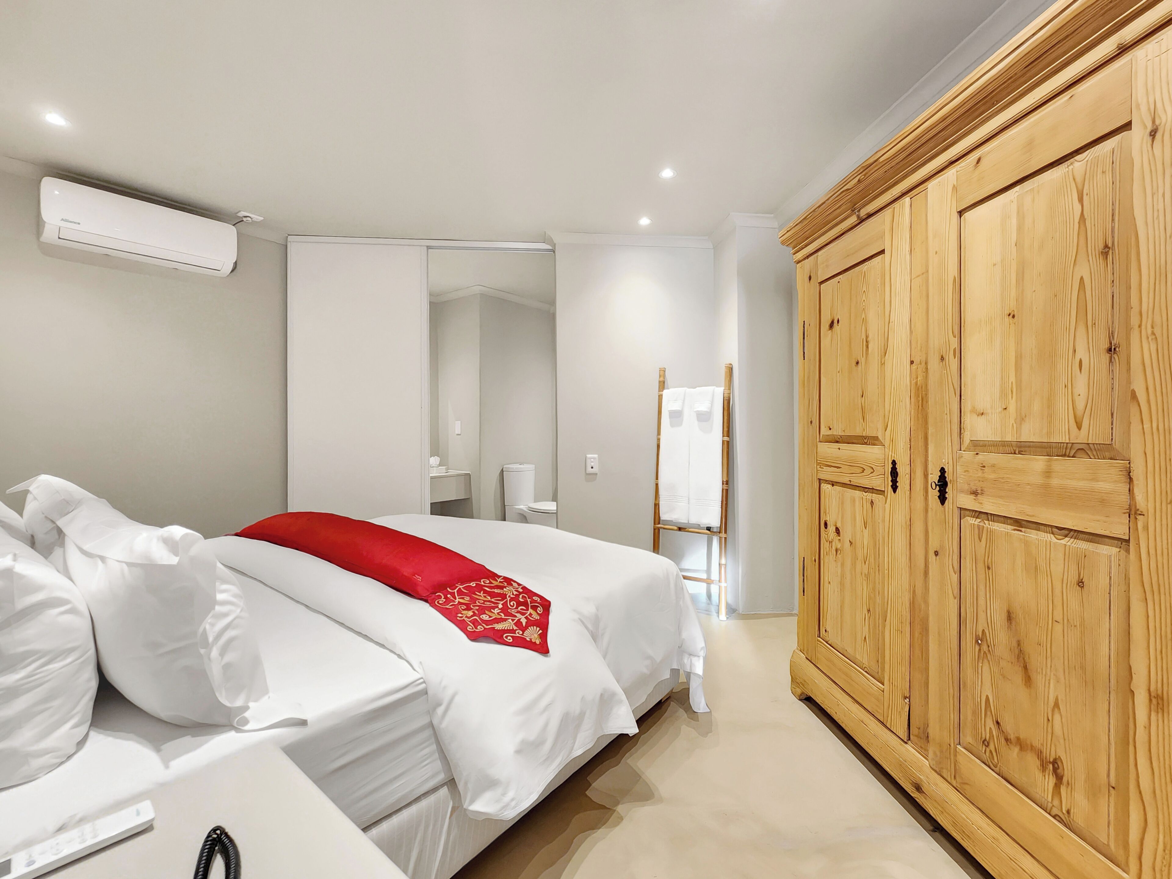 A hotel room with a bed, a wardrobe, a mirror, and an air conditioning unit.
