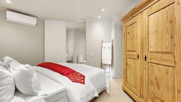 A hotel room with a bed, a wardrobe, a mirror, and an air conditioning unit.