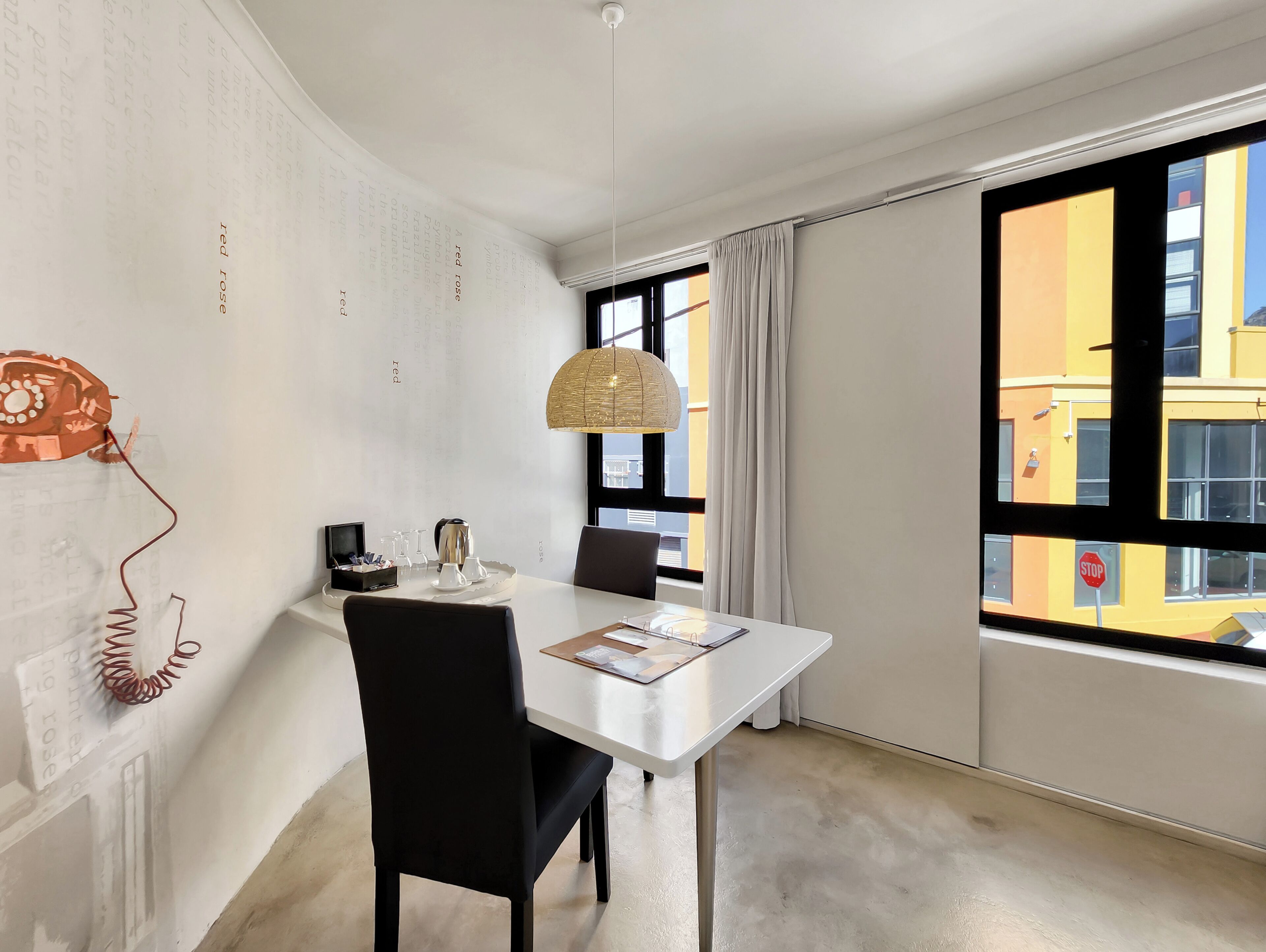 Een moderne kamer met een eettafel, stoelen, een hanglamp en uitzicht op een geel gebouw door een raam.