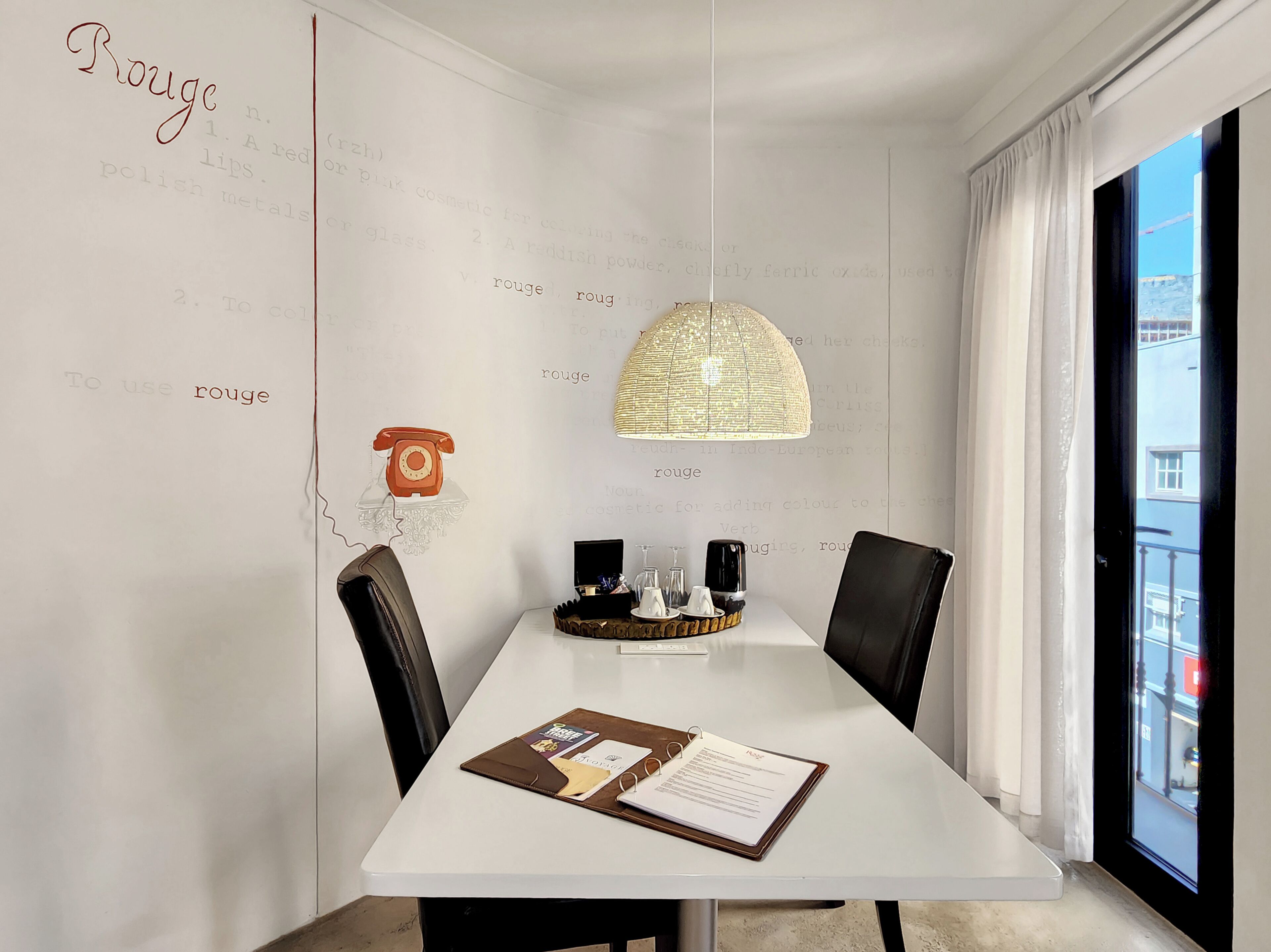 A modern dining area with a white table, black chairs, a pendant light, and a wall with text and a telephone.