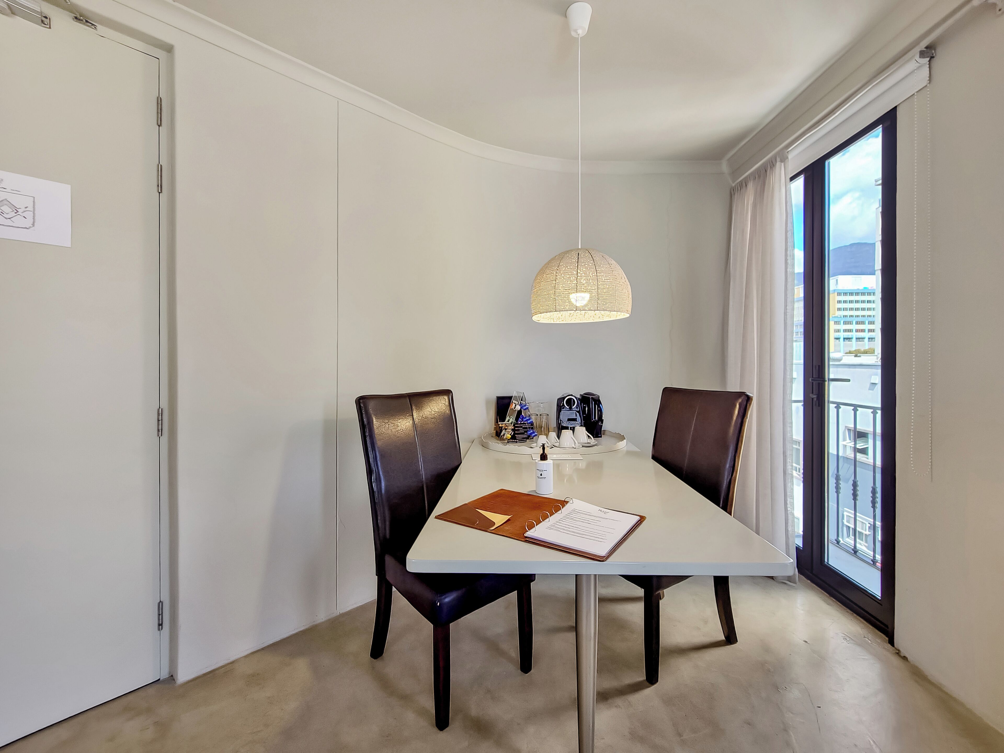 A dining area with a table, chairs, a pendant light, and a view through a window.