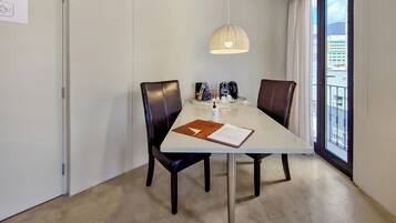 A dining area with a table, chairs, a pendant light, and a view through a window.