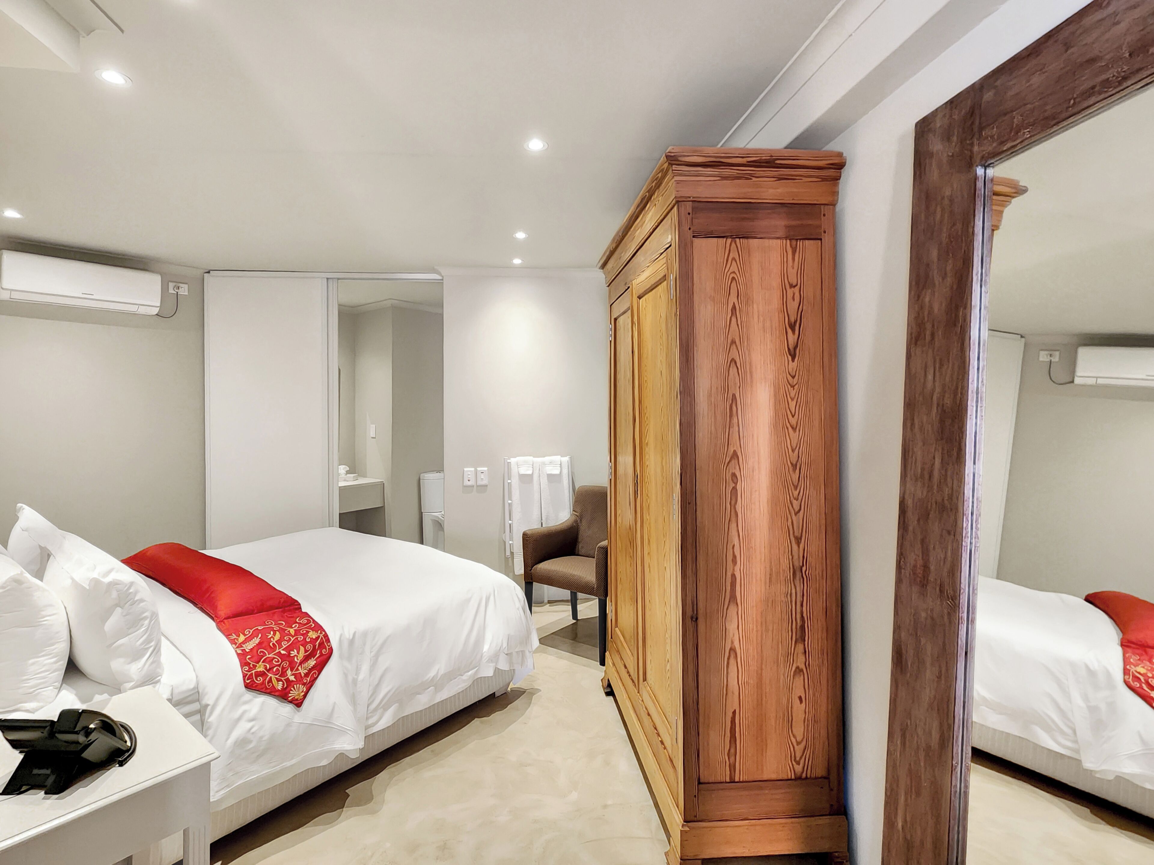A hotel room with a bed, a wooden wardrobe, a chair, a desk, and a mirror.